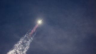 a large silver rocket flies through a blue sky above a column of flame