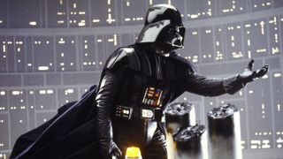 Darth Vader holds out his left hand as though he is about to pick an apple from a tree. But he isn't, he's in a technological setting with large circuit boards behind him.