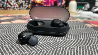 A black pair of Sony WF-C500 earbuds with their charging case on a lined material surface.