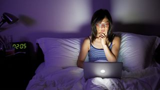 Woman awake at night on her laptop, clock shows it's 2am