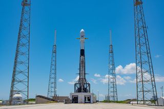 A white and black SpaceX Falcon 9 rocket with used booster stands atop the launch pad.