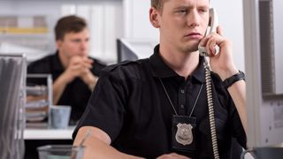 A police officer seated at a desk speaking on a landline telephone.