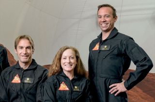 three smiling people inside a mock mars base