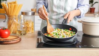 A pan shaking ingredients held over a glass stove top