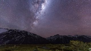 the bulge of the Milky Way stretches up from behind snow-capped mountains through a sky filled with stars.