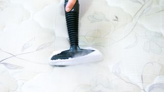 Person steam cleaning a white mattress to get rid of bed bug residue