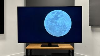 Samsung QN95D Neo-QLED TV on wooden TV stand with screen showing moon