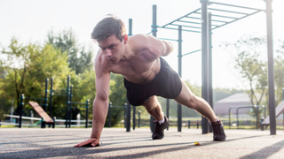 Man performing one-arm push-up outdoors with right hand down and left arm behind back