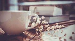 Books casually piled on a coffee table with a white mug