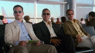 From left to right: Matt Damon, George Clooney, and Brad Pitt sitting in an airport. They're all wearing sunglasses and looking to the left.