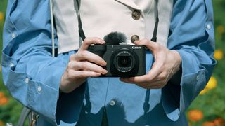 Canon PowerShot V1 vlogging compact in the hand, user wears blue jacket outdoors