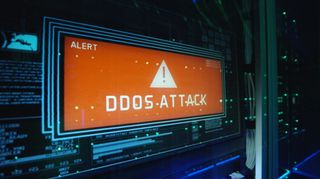 The words &#039;DDoS Attack&#039; displayed in an orange box on a monitor embedded in a series of rack-mounted servers.