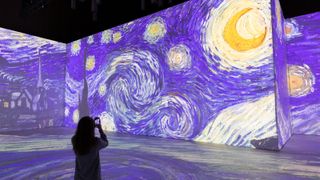 A woman standing in a room with Starry Night projected onto the walls