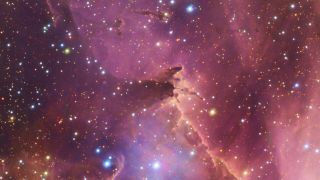 A section of space, awash with pink nebulous clouds, spattered with countless shining points of varying size and color.