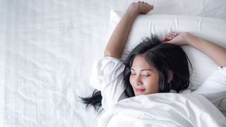 A woman sleeps happily with her arm raised on a comfortable organic mattress