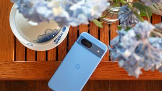 The blue Google Pixel 8a on a tea tray with blue hydrangeas above it