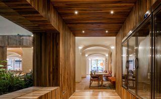 A restaurant with decorated tables, chairs, wooden walls, glass cabinet built into the wall and a plant feature.