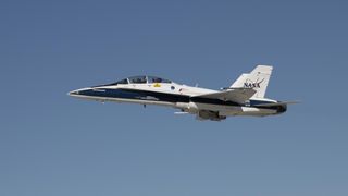 a blue and white fighter jet with the NASA logo flies through open sky