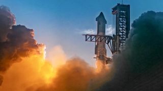 The top of a giant steel rocket just after liftoff next to its black launch tower. Smoke glowed with orange billows beneath, filling the frame on both sides.