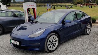 A photo of a tesla model 3 at a supercharger