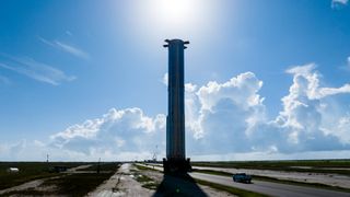 ground-level view of a large cylindrical rocket rolling along a road, with blue skies in the background.