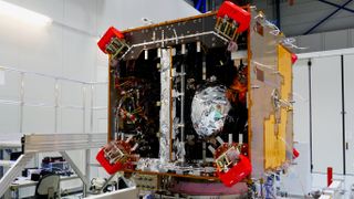 A cubical satellite under assembly in a clean room.