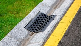 Water flowing into a drain next to a lawn