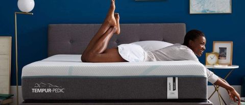A woman lays on top of the Tempur-Pedic Tempur-Adapt mattress, which is set against a dark blue bedroom 