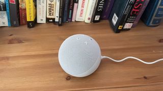 The Amazon Echo Dot 5th Gen on a wooden surface in front of some books.