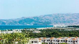 Martil beach, Morroco. White buildings and trees in the foreground with a beach scene in the middle of the image and then large hills and mountains in the background.