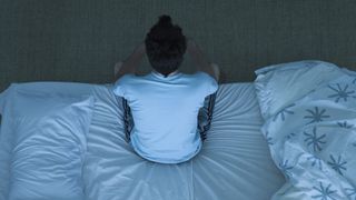 A man sits on the edge of his bed because he can't sleep