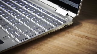 The HP Spectre x360 on a wooden desk showing off its ports and part of its keyboard