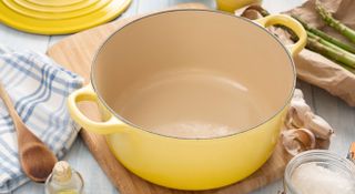 An empty yellow Dutch oven with the lid removed sitting on a chopping board surrounded by ingredientsh