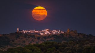 a full moon glows orange at dusk over a castle on a hill