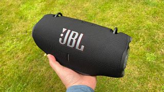 JBL Xtreme 4 wireless speaker held in hand above grassy lawn