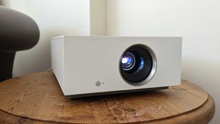 De bedste projektorer: En hvid LG CineBeam HU710PW sidder på et lille sofabord i et hjørne.