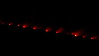 Scattered fragments of comet Shoemaker-Levy 9 appear as a series of bright red dots with varying brightness 'tails' against a black background.