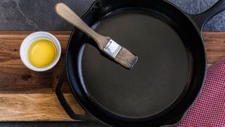 Cast iron skillet coated with cooking oil with a wooden handled brush