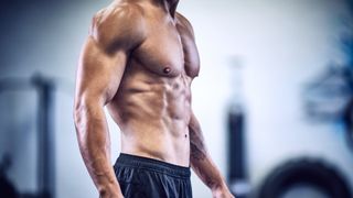 Man standing with top off showing muscled torso from side