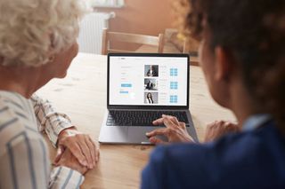 Mature female nurse teaching senior woman booking appointment on laptop at home