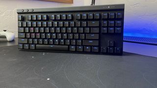 The Logitech G515 LIGHTSPEED TKL gaming keyboard standing on a black desk next to a game controller