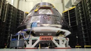 cone-shaped spacecraft mounted on a circular-shaped stand. behind are black panels