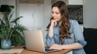 A woman smiling while using a MacBook at a desk.