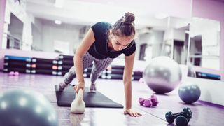 a woman performing a plank with a kettlebell pull through