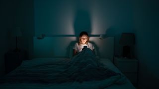 Mujer agotada y somnolienta tumbada en la cama usando el smartphone, no puede dormir. Insomnio, concepto de adicción. Chica triste aburrido en la cama desplazándose a través de las redes sociales en el teléfono móvil a altas horas de la noche en el dormitorio oscuro.