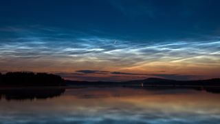 Noctilucent clouds above a lake with a perseid meteor streaking through the sky.