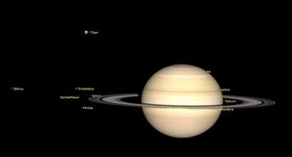 Saturn hangs in black space gourged with horizontal rings. Some moons are nearby.