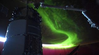 an aurora reaching into space from earth. a robot arm and a module are in the front, in shadow