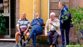 Four elderly men sit and talk on a bench