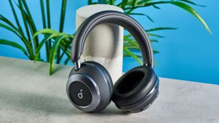 the soundcore space one pro headphones; a photograph of a pair of black over-ear headphones with cushioned cups and a soft headband, photographed in front of a blue background